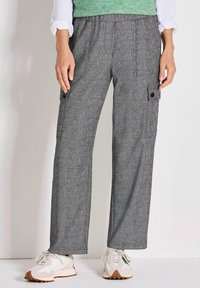 Grau gemusterte Cargo-Hosen mit lockerer Passform, ausgestattet mit Seitentaschen und einem dehnbaren Bund, kombiniert mit weißen und beigen Turnschuhen.