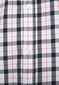 Camicia a scacchi bianco e nero con accenti rossi, realizzata in tessuto dalla trama liscia, con un bottone al centro.