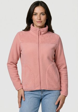 Frau trägt eine pinkfarbene Fleecejacke mit durchgehendem Reißverschluss, hohem Kragen und zwei strukturierten Fronttaschen, kombiniert mit hellblauen Jeans.