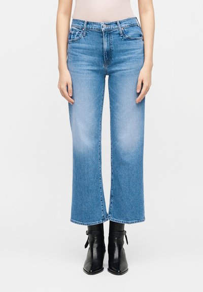 Γυναίκα με ψηλόμεσο, ανοιχτό μπλε cropped flare τζιν με ξεθωριασμένα γόνατα και μαύρα μποτάκια με μυτερή μύτη.