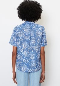Camicia a maniche corte con motivo floreale blu e contorni bianchi, vestibilità rilassata, dettaglio sulla spalla posteriore e orlo curvo.