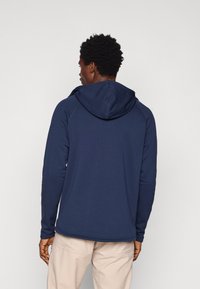 Tumesinine kapuutsiga sviiter, raglanvarrukate ja sileda tekstuuriga. Omab reguleeritavat paelavõttu ja kontrastset õmblusdetaili.