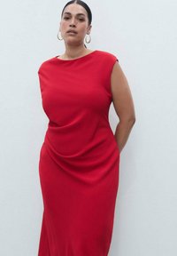 Rotes, ärmelloses Kleid mit hohem Kragen; weicher, fallender Stoff. Besitzt einen lockeren Schnitt und eine glatte Textur. Runde Ohrringe als Akzent.