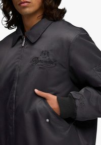 Bomber in satin nero con zip frontale, polsini a coste e logo "Represent" ricamato. Presenta due tasche laterali e una finitura elegante.