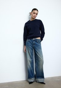 Maglione blu navy con scollo rotondo, abbinato a jeans a gamba larga azzurri slavati con una lavatura più chiara all'orlo e tacchi neri a punta.