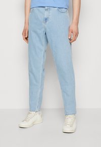 Jeans de denim azul claro con un corte relajado, que cuentan con una cinturilla estándar y costuras visibles. Combinados con zapatillas blancas.