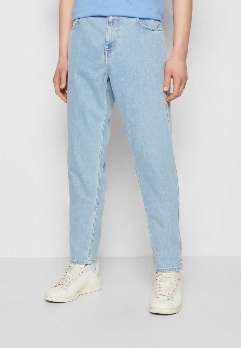 Jeans de denim azul claro con un corte relajado, que cuentan con una cinturilla estándar y costuras visibles. Combinados con zapatillas blancas.