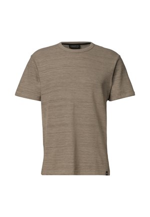Homme aux cheveux courts et foncés portant un t-shirt marron clair à manches courtes et col rond, debout devant un fond clair uni.