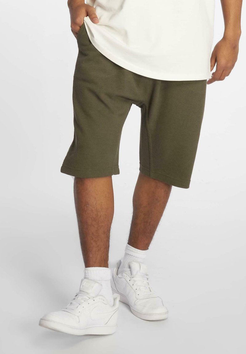 Groene shorts met een gestructureerd, geribbeld patroon, met een relaxte pasvorm, zijzakken en een zoom die boven de knie valt. Gecombineerd met witte sneakers.