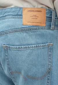 Ανοιχτό μπλε τζιν τζιν με δερμάτινη ετικέτα στη μέση, που φέρει το όνομα της μάρκας "JACK & JONES" και ραφές κατά μήκος των πίσω τσεπών.
