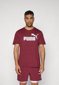 Mørkerød sports T-shirt med hvid 'PUMA' logo, rund hals, kortærmet, parret med matchende shorts med side-splits og hvid kant.