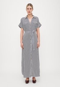 Vestido maxi listrado com mangas curtas, frente com botões, dois bolsos no peito e um cinto amarrado na cintura, nas cores preto e branco, em tecido suave.
