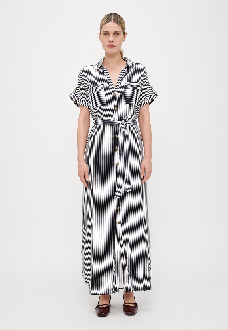 Vestido maxi listrado com mangas curtas, frente com botões, dois bolsos no peito e um cinto amarrado na cintura, nas cores preto e branco, em tecido suave.