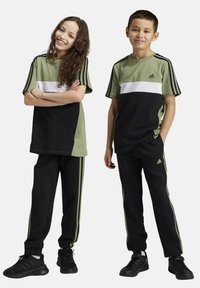Conjunto deportivo en verde y negro que incluye una camiseta de manga corta con una franja blanca y pantalones negros con franjas laterales verdes, confeccionado en tejido transpirable.