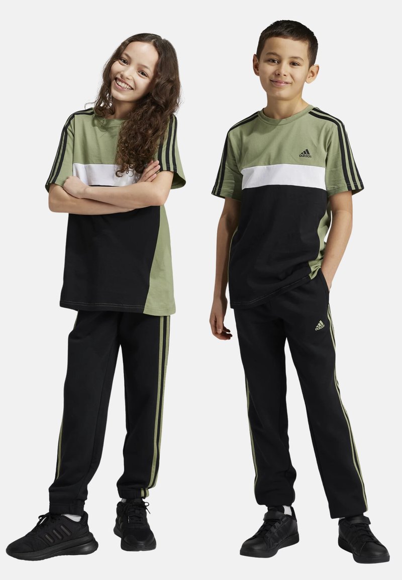 Conjunto deportivo en verde y negro que incluye una camiseta de manga corta con una franja blanca y pantalones negros con franjas laterales verdes, confeccionado en tejido transpirable.