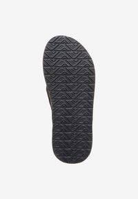 Semelle de chaussure en caoutchouc noir avec un motif en zigzag texturé pour l'adhérence, présentant un bord lisse et sans marquages ou logos visibles.