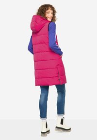 Lång, rosa puffväst med huva, med ett quiltat mönster. Bärs över en blå långärmad topp, tillsammans med blåjeans och vita stövlar.