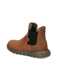 Botte de cheville en suède marron avec un panneau latéral élastique noir, un col à motifs et une semelle en caoutchouc flexible avec un design en vagues.