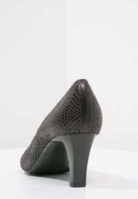 Chaussure à talon haut noire avec un dessus en maille texturée, un bout pointu et un talon carré. Accents en cuir lisse à l'arrière et sur les bords.