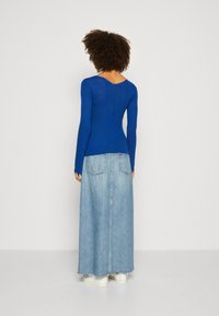 Blå tettsittende langermet topp med strukturert strikkedesign, kombinert med en lys blå denim maxiskjørt med lommer. Hvite joggesko synlige.