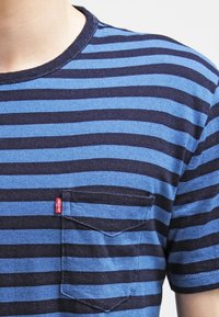 Blå och marinrandig T-shirt i bomull, med en ficka på vänster sida och rundad halsringning med korta ärmar.