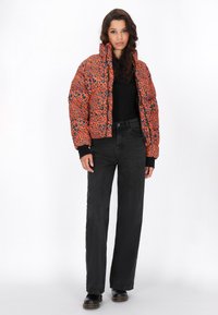 Pufi bunda v oranžové barvě s modrým leopardím potiskem, zkrácený střih, elastické manžety, v kombinaci s černými džínovými kalhotami s vysokým pasem a černými botami.