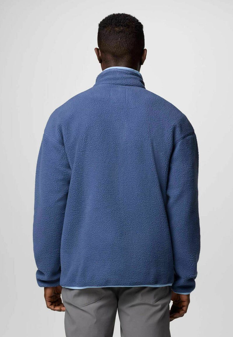 Niebieski polarowy sweter z wysokim kołnierzem, teksturowaną powierzchnią i długimi rękawami. Widok z tyłu pokazuje luźny krój z jasnoniebieskimi akcentami.