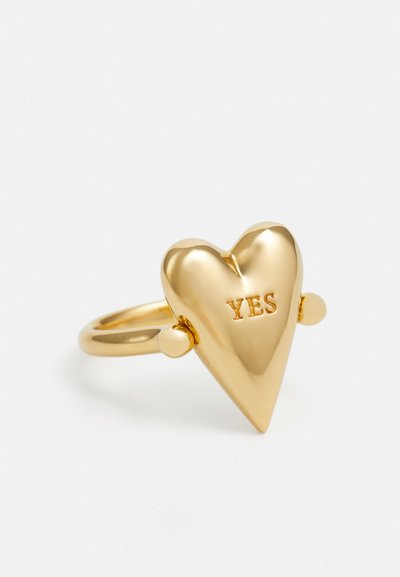 Goldfarbener, herzförmiger Ring mit polierter Oberfläche und dem Wort "JA" eingraviert. Verfügt über zwei kleine, runde Akzente auf beiden Seiten.