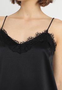 Top de satén negro con encaje en el escote en forma de V y tirantes finos. Textura suave con un diseño fluido que resalta el escote.