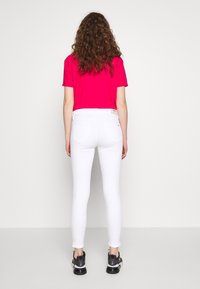 Jeans blancos ajustados combinados con una camiseta de color rosa brillante. Los jeans tienen un diseño clásico de cinco bolsillos y se complementan con zapatillas negras.