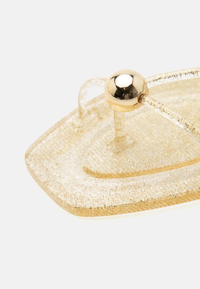 Sandale flip-flop transparente cu sclipici auriu, cu un post din aur solid sferic pentru deget și bretele transparente și sclipitoare, pe fundal alb.