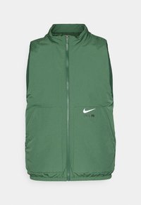 Grön ärmlös zip-up Nike väst med två frontfickor och vit Nike Air-logotyp på vänster sida.
