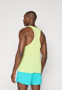 Débardeur de sport en tissu mesh vert clair, avec un design dos nageur et des fentes sur les côtés. Associé à un short de sport turquoise.