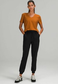 Pomarańczowa koszulka z dekoltem w serek, czarne dresowe spodnie z elastycznym pasem i bocznymi kieszeniami oraz czarno-białe trampki. Prosty, codzienny strój.