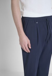 Tamno plave hlače sa opuštenim krojem, s elastičnim pojasom, vezicom i dva prednja nabora. Glatka tekstura, minimalistički dizajn.