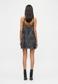 Μαύρο φόρεμα με φράντζες, λεπτές τιράντες, στρωματοποιημένη υφή και φερμουάρ στην πλάτη. Συνδυασμένο με μαύρες μυτερές μποτάκια μέχρι τον αστράγαλο.
