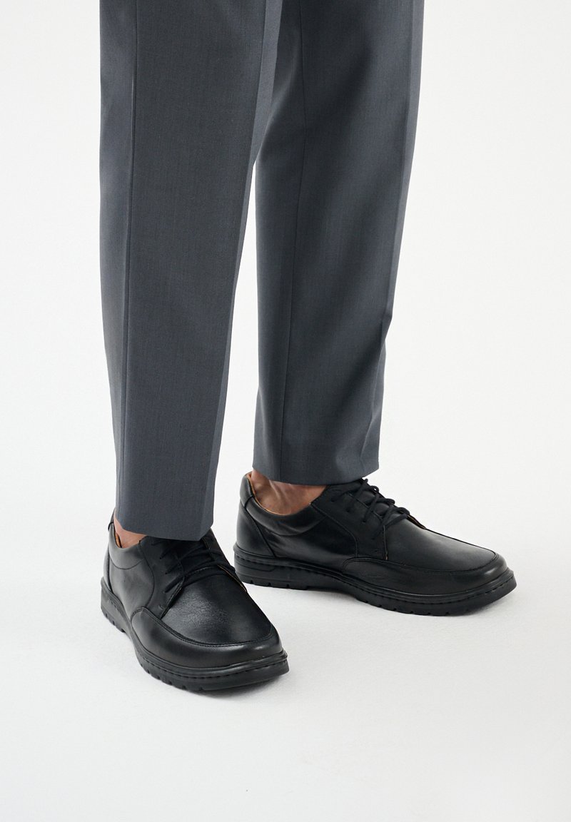 Scarpe in pelle nera con una superficie liscia, design con lacci e punta arrotondata. Abbinate a pantaloni grigi su misura.