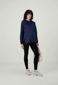 Sudadera con capucha de color azul oscuro, de corte holgado y con cordón, combinada con leggings negros y zapatillas de color claro. Un look casual con detalles mínimos.
