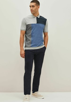 Polo de bloques de color con paneles en gris, azul marino y azul; mangas cortas, cuello, tejido texturizado; combinado con pantalones oscuros y zapatillas claras.
