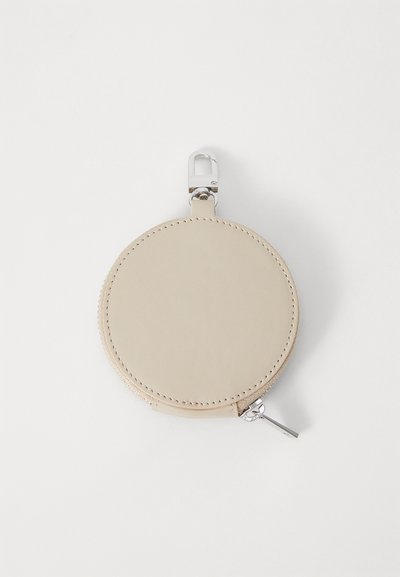 Bolsita redonda de cuero beige con cremallera plateada, costuras expuestas y un clip giratorio para sujeción. Textura suave, diseño minimalista.