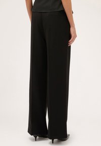 Pantalones negros de cintura alta con una silueta de pierna ancha, fabricados en un tejido suave, con bolsillos laterales visibles y detalles de costura sutiles en la parte posterior.