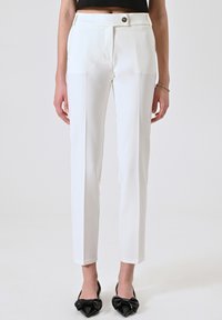 Pantalons blancs ajustés avec une coupe slim, poches latérales et une fermeture à bouton unique à la taille. Tissu lisse avec un détail de pli.