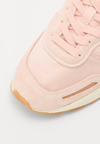Heledalt roosa sneaker, millel on nahk ja võrk, tekstuuriga pind, ümmargune varvas ja pruun kummist tall. Sidemed on samas toonis.