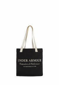 Borsa tote in tela nera con due manici color crema, caratterizzata da un testo bianco audace: "UNDER ARMOUR Origine dei Performance FONDATO NEL 1996."