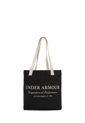 Schwarze Canvas-Shopper-Tasche mit zwei cremefarbigen Griffen, die auffälligen weißen Text trägt: "UNDER ARMOUR Ursprünge der Leistung GEGRÜNDET 1996."