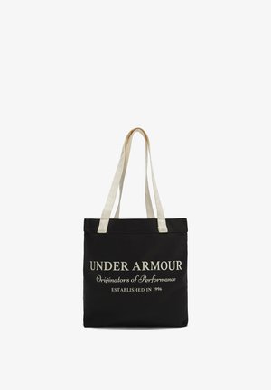 Schwarze Canvas-Shopper-Tasche mit zwei cremefarbigen Griffen, die auffälligen weißen Text trägt: "UNDER ARMOUR Ursprünge der Leistung GEGRÜNDET 1996."