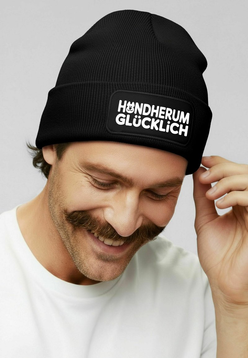 Black knitted beanie with a ribbed texture, featuring a rectangular patch displaying the text "HUNDHERUM GLÜCKLICH" in bold white letters.
