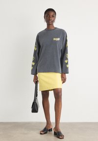 Gray long-sleeve sweatshirt with yellow heart pattern, paired with a yellow skirt. Accessorized with a black handbag and slide sandals.