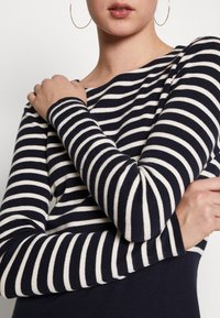 Haut à rayures bleu marine et blanc à manches longues avec un décolleté bateau et une texture tricot douce, avec des manches ajustées et une silhouette près du corps.