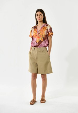 Bloemige shirt met korte mouwen in oranje, roze en bruine patronen, gecombineerd met tan shorts. De shorts hebben een relaxte pasvorm en twee zijzakken.